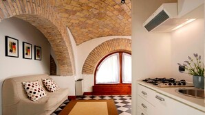 A cozy living room with a checkered floor, a sofa with polka dot cushions, a fireplace, and a kitchen with a gas stove. - Roma Resort Termini (Rome)