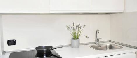 Una cocina moderna con una placa de inducción negra, un lavamanos de acero inoxidable y una planta de lavanda en maceta.