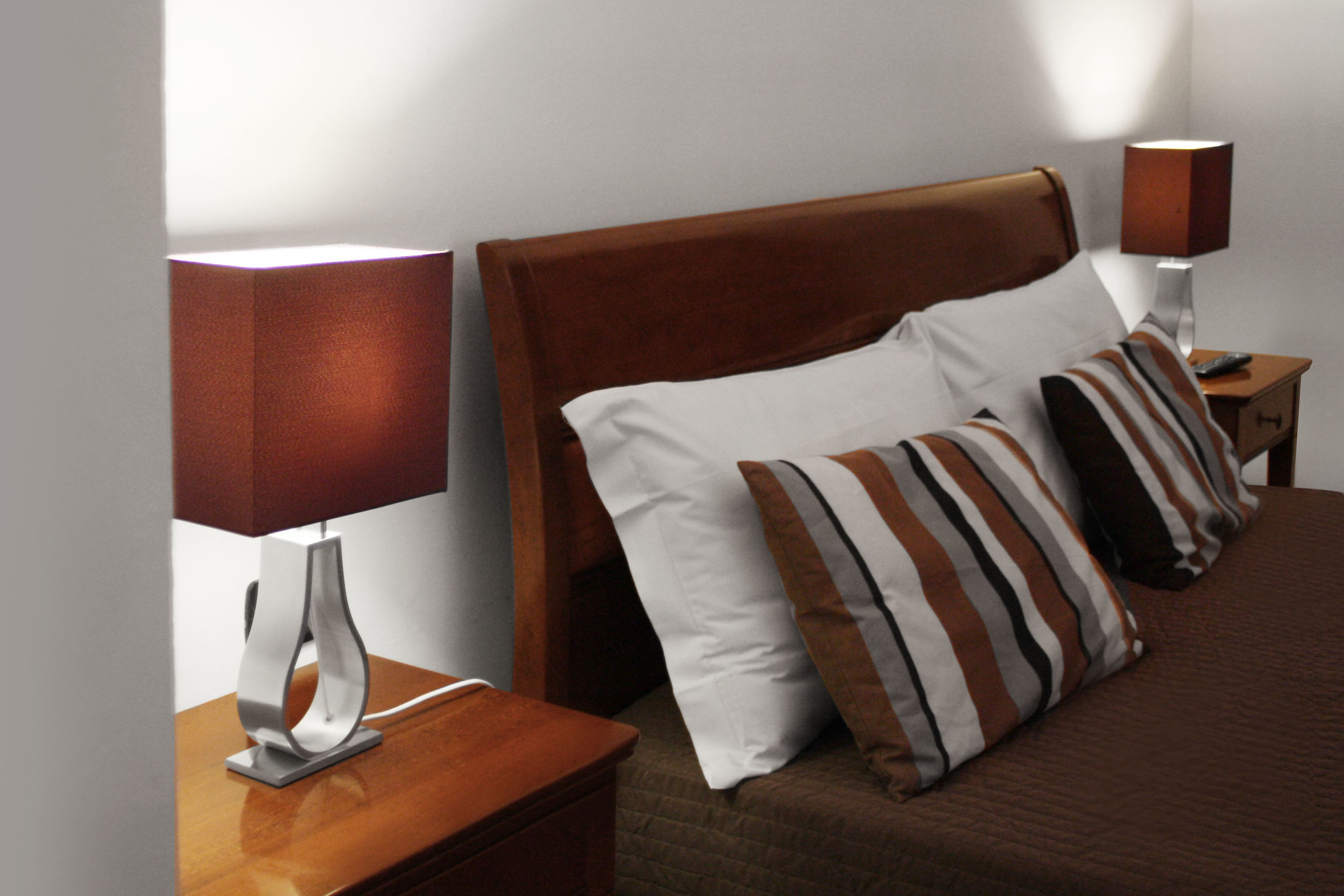 A neatly made bed with striped pillows and a wooden headboard, flanked by two bedside tables with lamps.