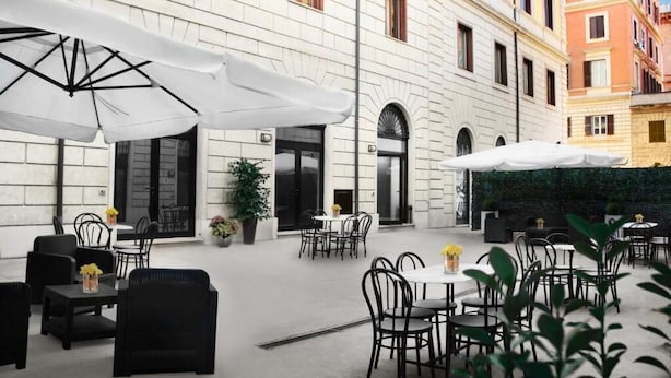 An outdoor cafe area with tables and chairs, white umbrellas, and a building facade. - Roma Resort Termini (Rome)
