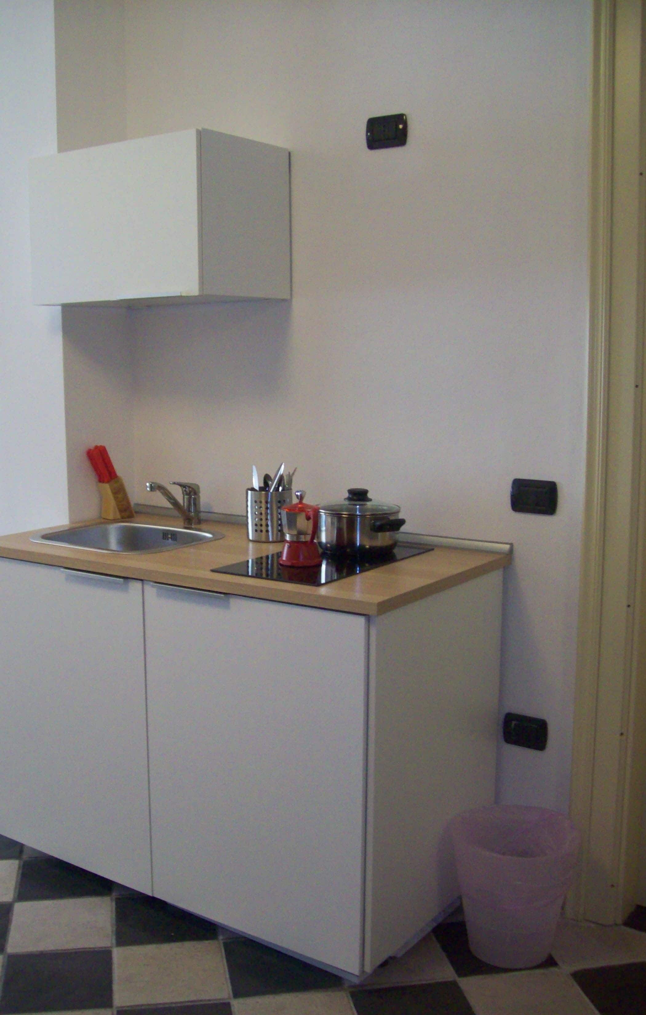 A compact kitchen with a sink, countertop, and cabinets. There is a trash bin and a wall-mounted light switch.