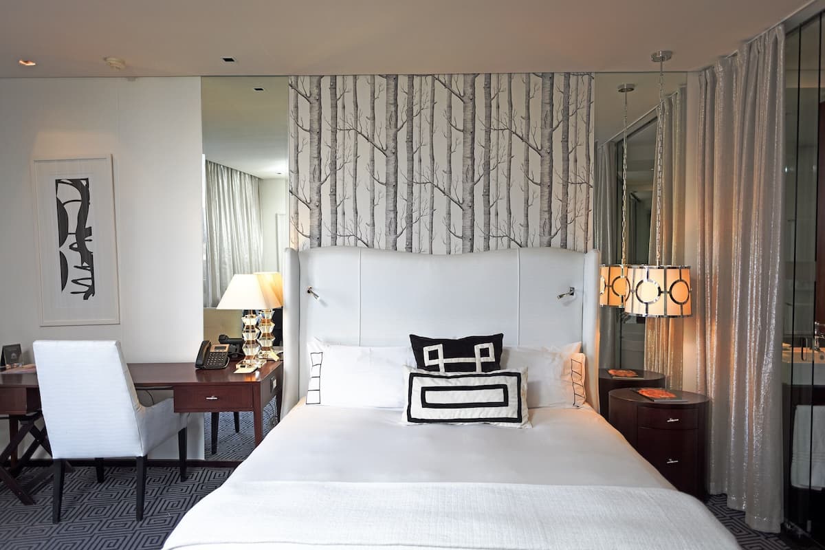Een hotelkamer met een groot bed, een bureau met telefoon, een stoel, een nachtkastje met lamp en een spiegel.
