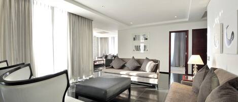 A modern living room with a sofa, armchairs, and a coffee table. There is a dining area in the background with a table and chairs.