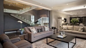 Una sala de estar moderna con una escalera, dos sofás, una mesa de centro y una planta grande.