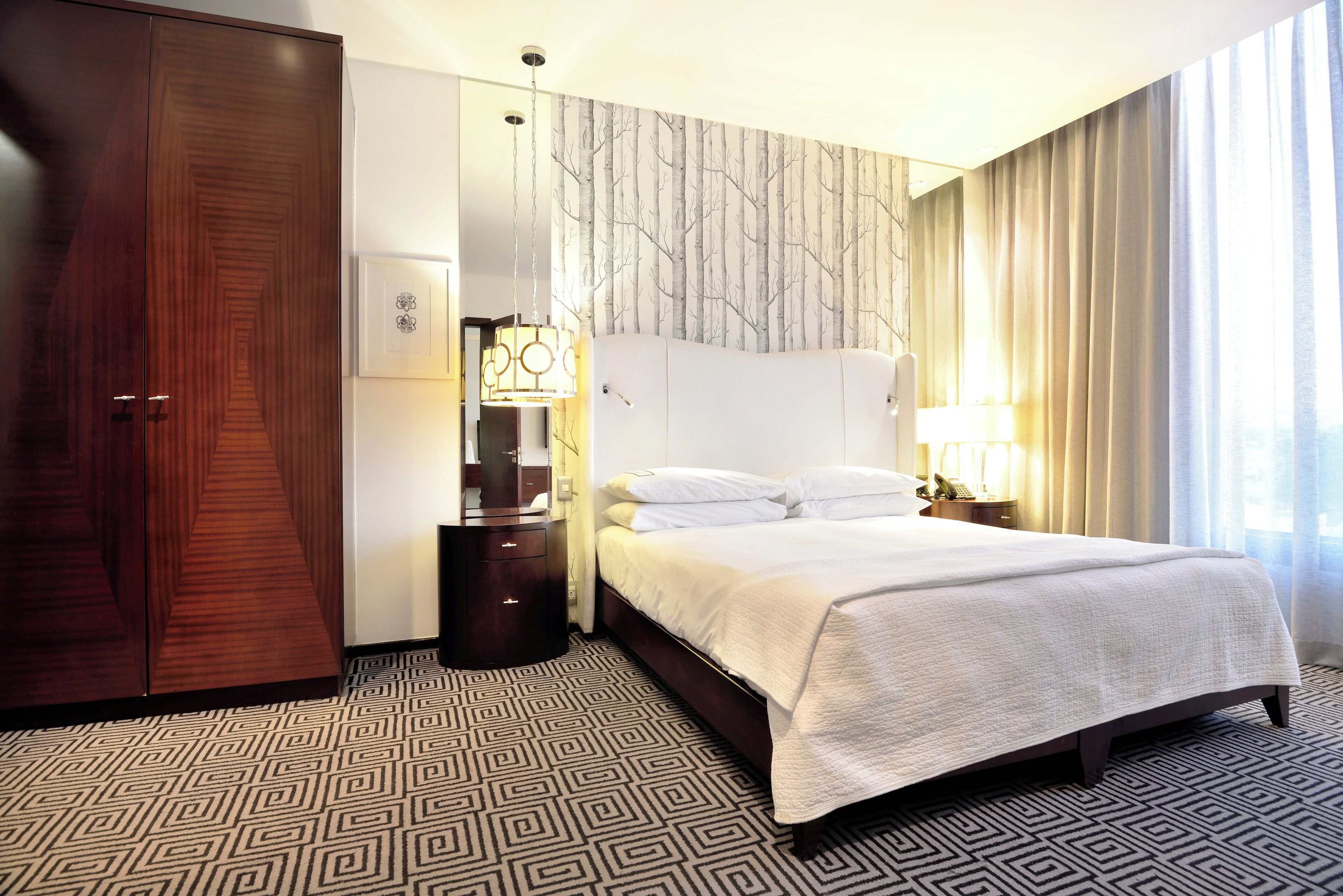 Een hotelkamer met een groot bed, een garderobe, een nachtkastje met een lamp en een kamerbreed tapijt met een patroon.