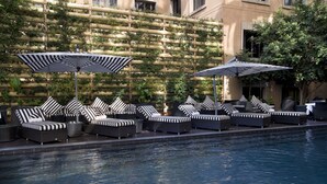 Un área al lado de la piscina con múltiples sillas de descanso y sombrillas, una piscina con baldosas y una pared con jardineras verticales.