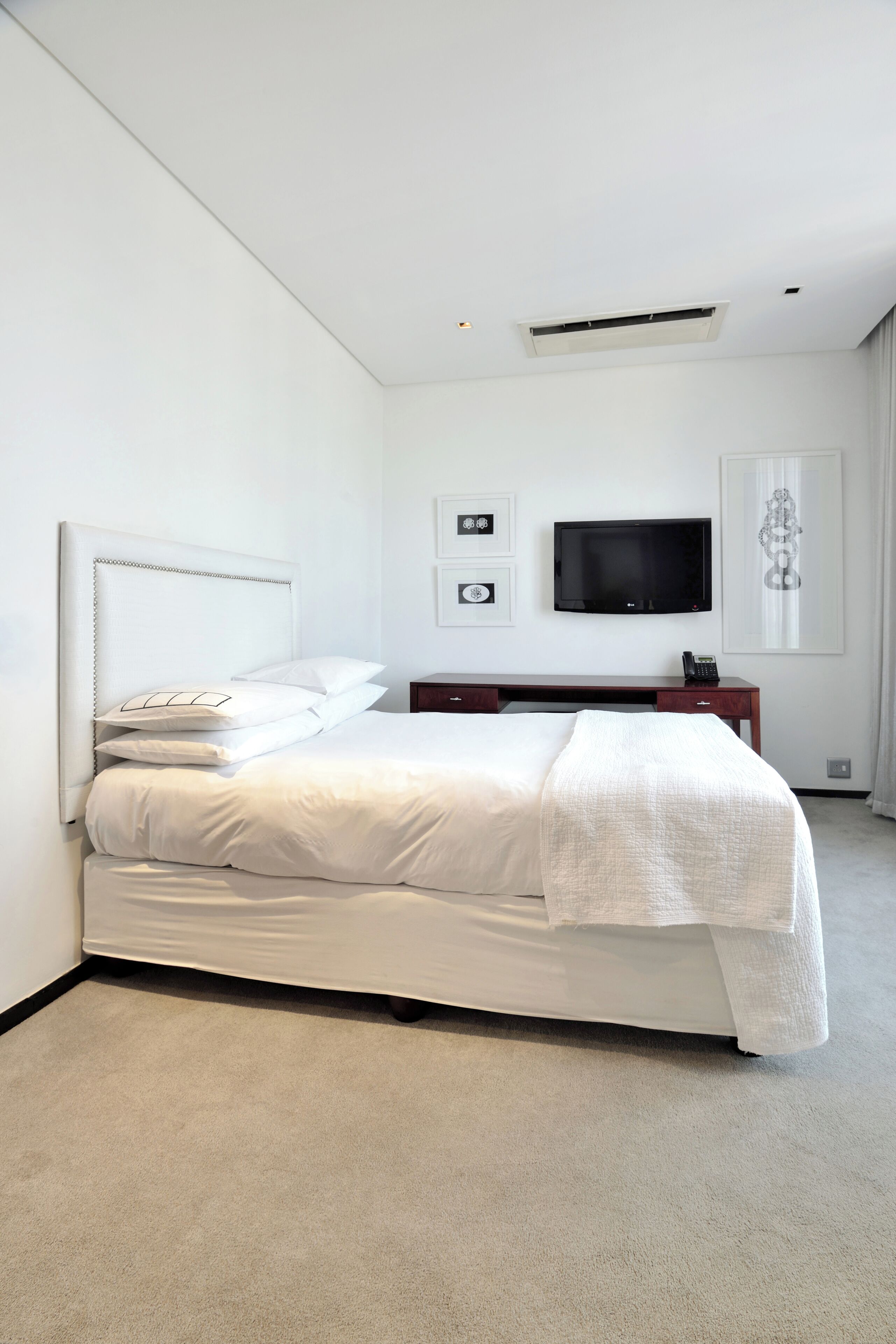 A modern hotel room with a large bed, a flat-screen TV mounted on the wall, a desk with a telephone, and a framed picture.