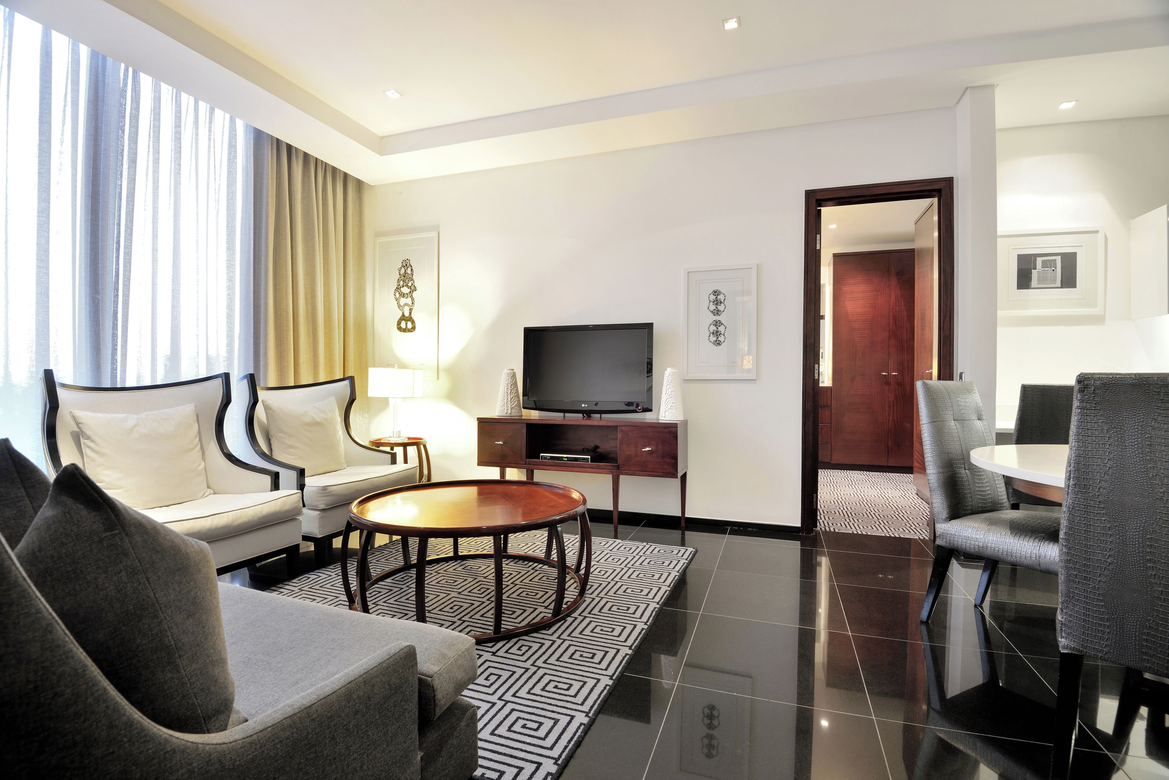 Une chambre d’hôtel moderne équipée d’un canapé, d’une table basse ronde, d’un téléviseur et d’un coin repas avec des chaises.