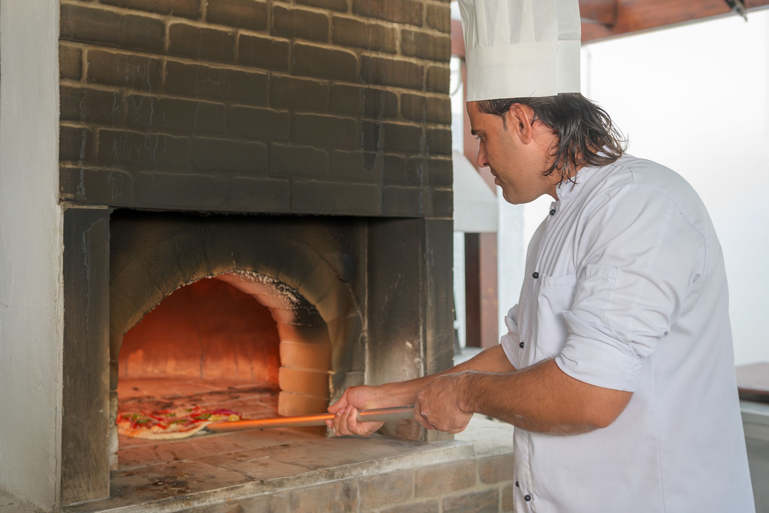En person bruger et langt værktøj til at håndtere en pizza i en murstensovn.