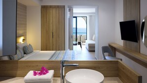 A modern hotel room with a large bed, a wooden vanity with a bowl sink, a flat-screen TV, and a balcony with a view of the sea. - Sunrise Hotel (Rhodes)