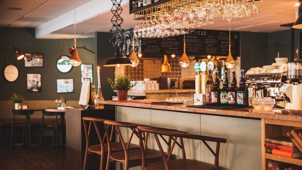 Zona de bar con taburetes de madera, copas de vino colgantes y una variedad de botellas.