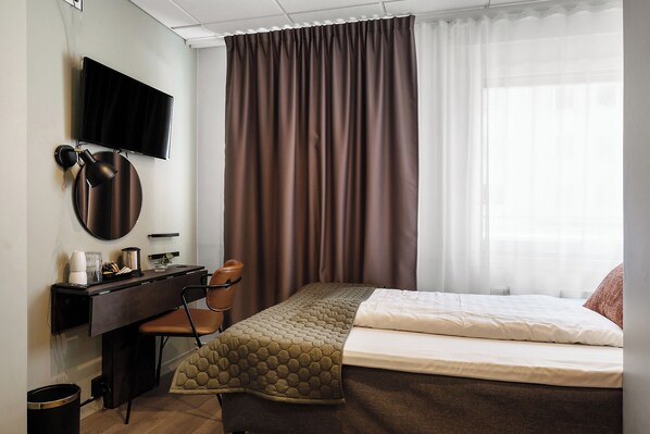 Une chambre d’hôtel avec un lit, un bureau et une chaise, une télévision et une fenêtre avec des rideaux.