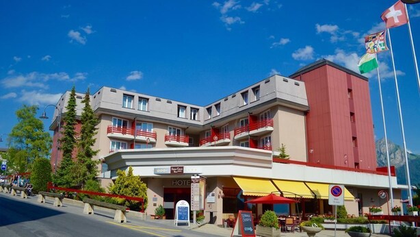 Un hôtel à la façade rouge et beige, doté de nombreux balcons et d’un mât sur lequel flottent des drapeaux.