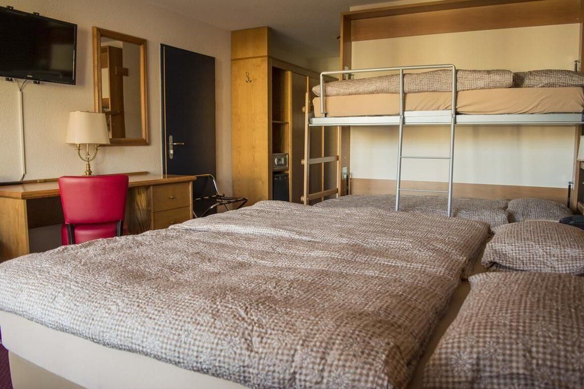Una camera d'albergo con un letto a castello, una scrivania con una sedia, una televisione e uno specchio.