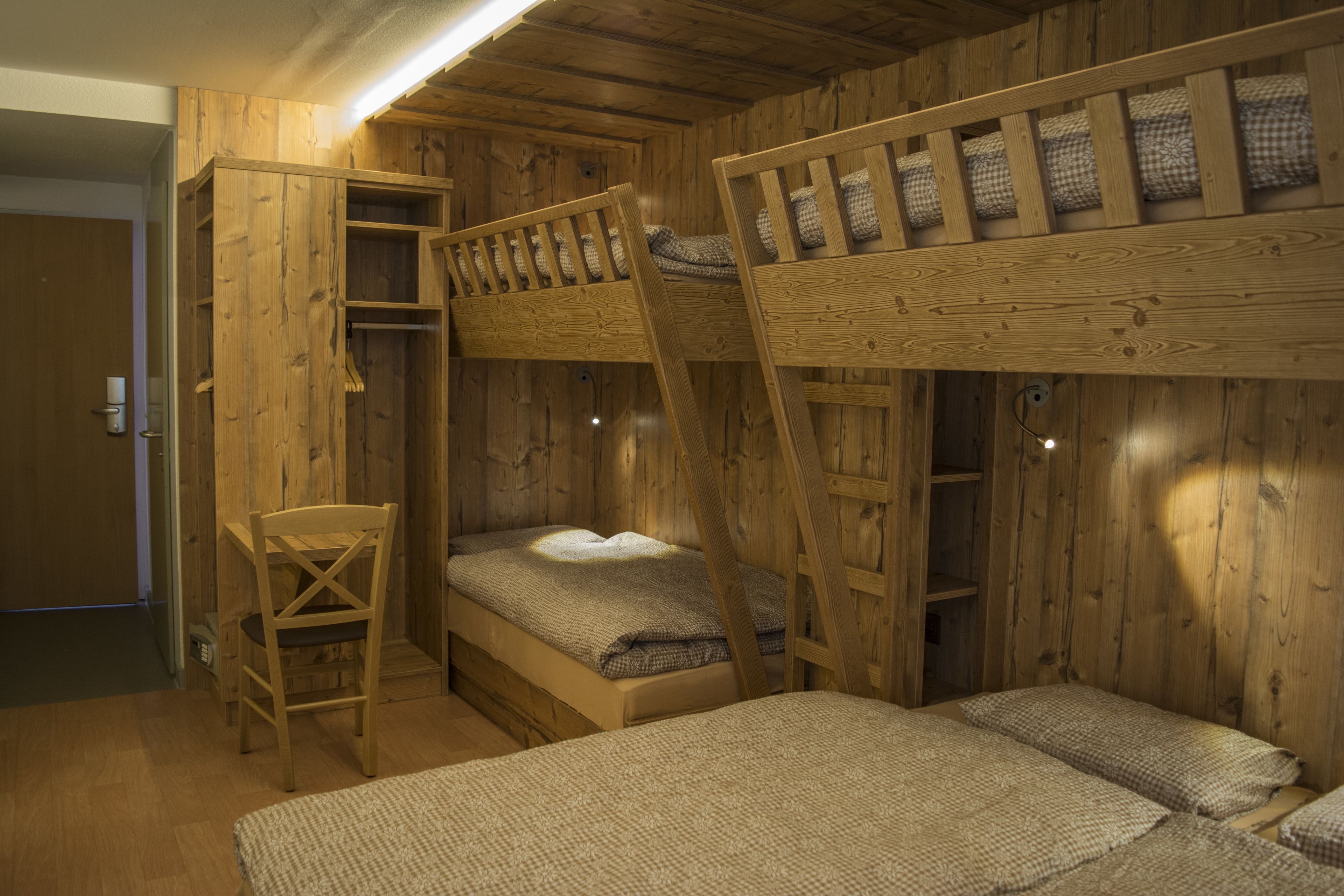 A bunk bed room with wooden walls and a desk.