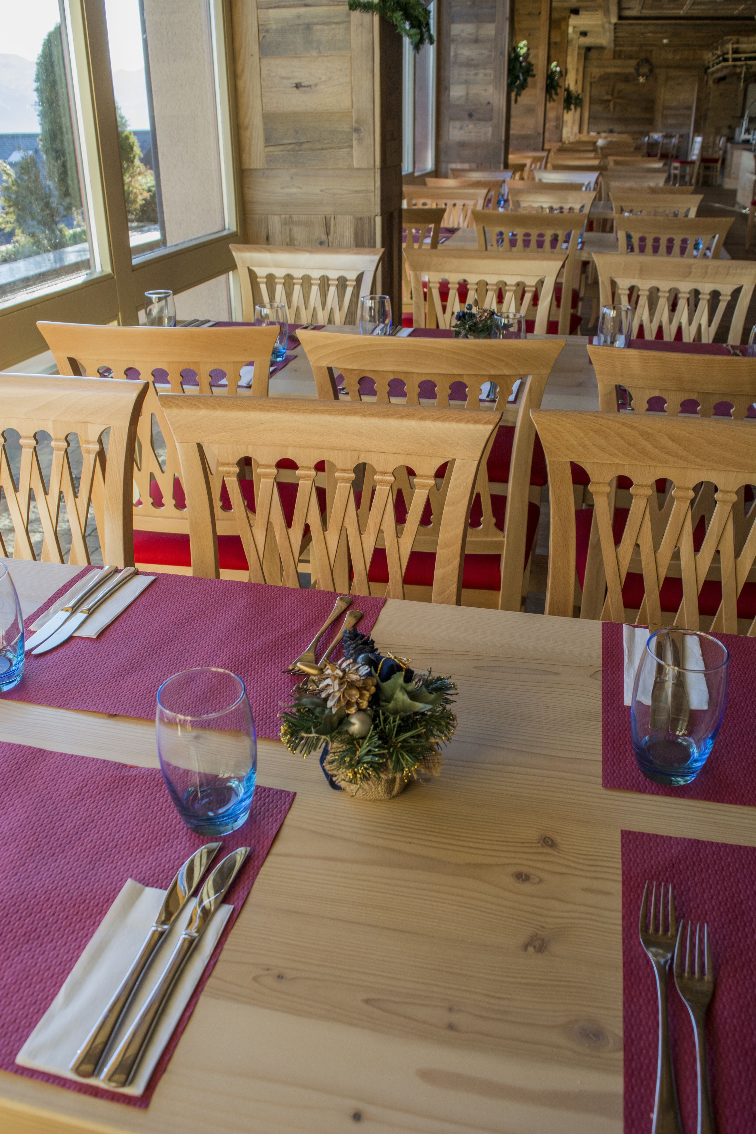 Un restaurante con mesas y sillas de madera, cada conjunto con cubiertos y servilletas.