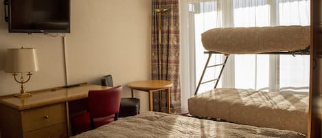 Una habitación de hotel con cama, escritorio, silla, televisor y ventana con cortinas.
