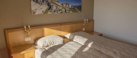 A bedroom with a wooden headboard, two bedside tables, a bed with a textured blanket, and a mountain landscape painting on the wall.