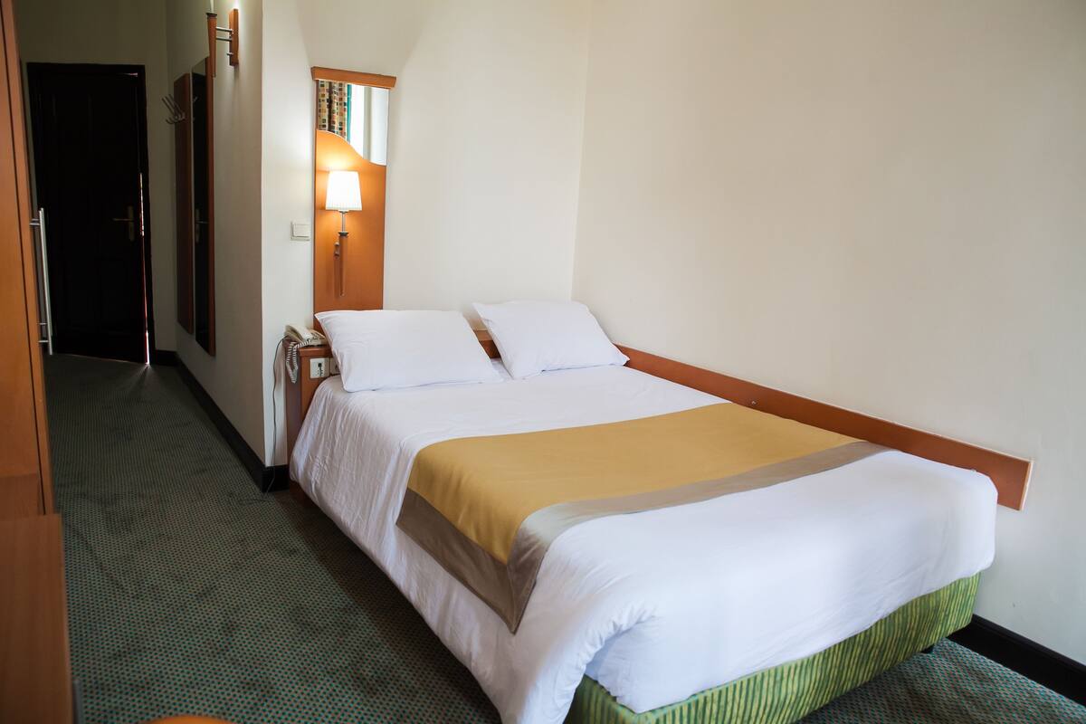 A hotel room with a single bed, a bedside lamp, and a telephone.