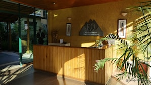 A reception desk with a wooden finish, a framed sign for the Gorilla Group, and a potted plant to the right. - Gorillas City Centre Hotel (Kigali)