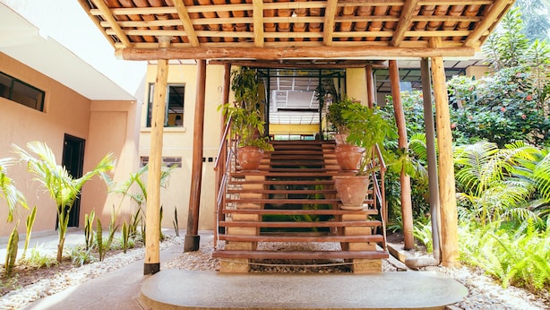 A wooden staircase with a tiled roof leading to a building entrance, surrounded by potted plants and greenery. - Gorillas City Centre Hotel (Kigali)