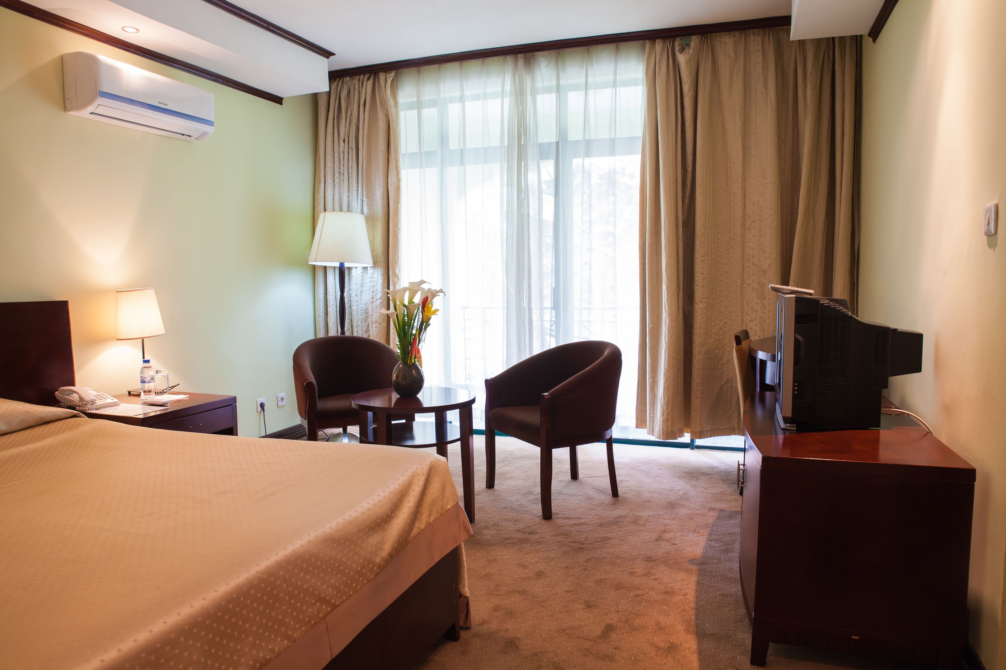 Habitación de hotel con cama, escritorio, silla, televisión y ventana con cortinas.