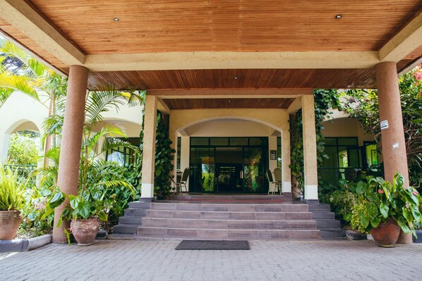 A covered entrance with a wooden ceiling, steps leading to a glass door, and potted plants around.