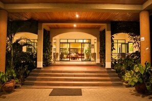 Entrada de un hotel con techo de madera, puertas de cristal y escalones que conducen a un comedor.