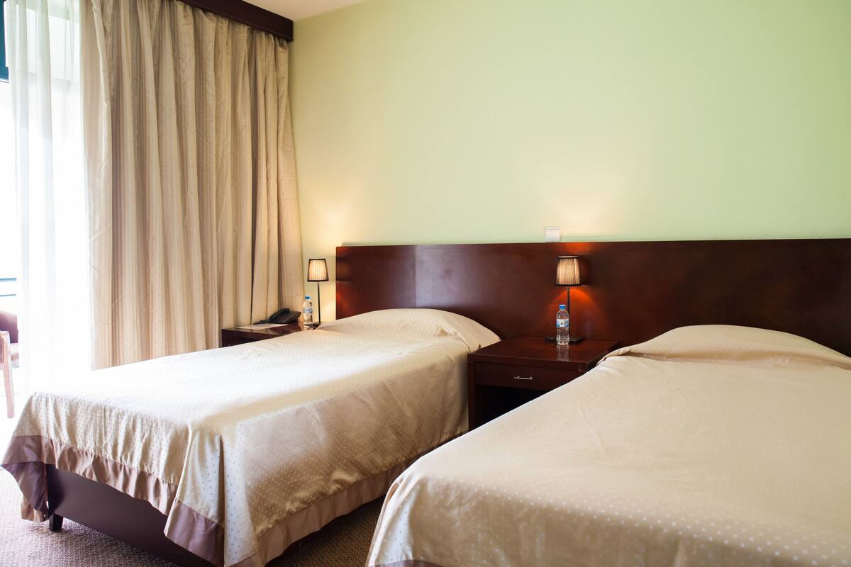 Une chambre d’hôtel avec deux lits, une table de chevet, une lampe et une fenêtre avec des rideaux.