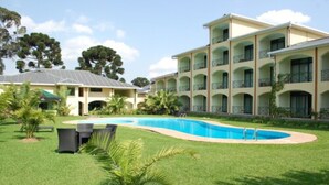 Un hotel con piscina rodeado por un césped cuidado y palmeras.