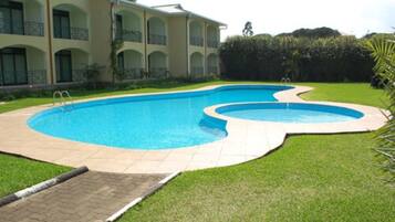 A swimming pool with a curved design, surrounded by a well-maintained lawn and a building with balconies.