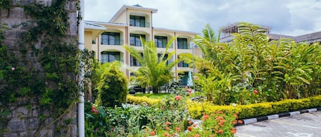 A hotel with a multi-story structure, a landscaped garden with various plants and flowers, and a paved parking area.