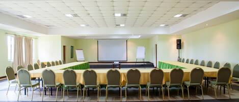 Une salle de conférence équipée d’une longue table et de chaises, d’un écran de projection et d’un tableau blanc.