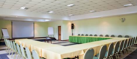 A conference room with a long table, chairs, a projector screen, and a whiteboard.