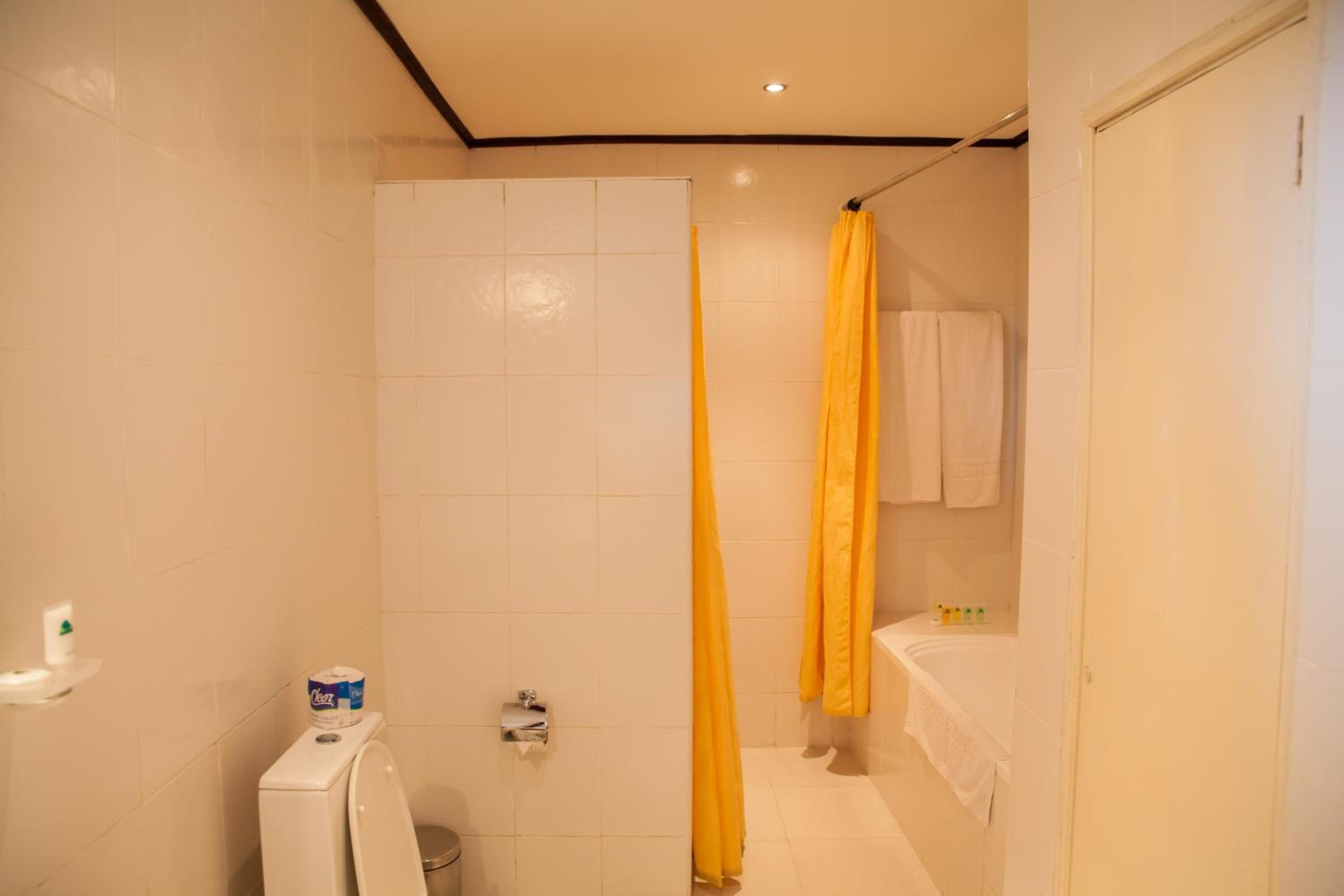 Un bagno con piastrelle bianche, un water, una tenda da doccia e una vasca da bagno.