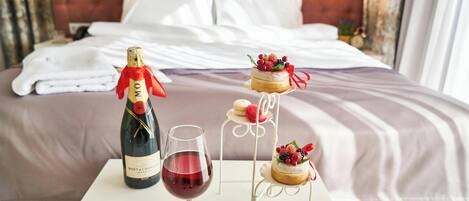 Una cama con sábanas blancas, una botella de champán y una copa de vino tinto sobre una mesa.