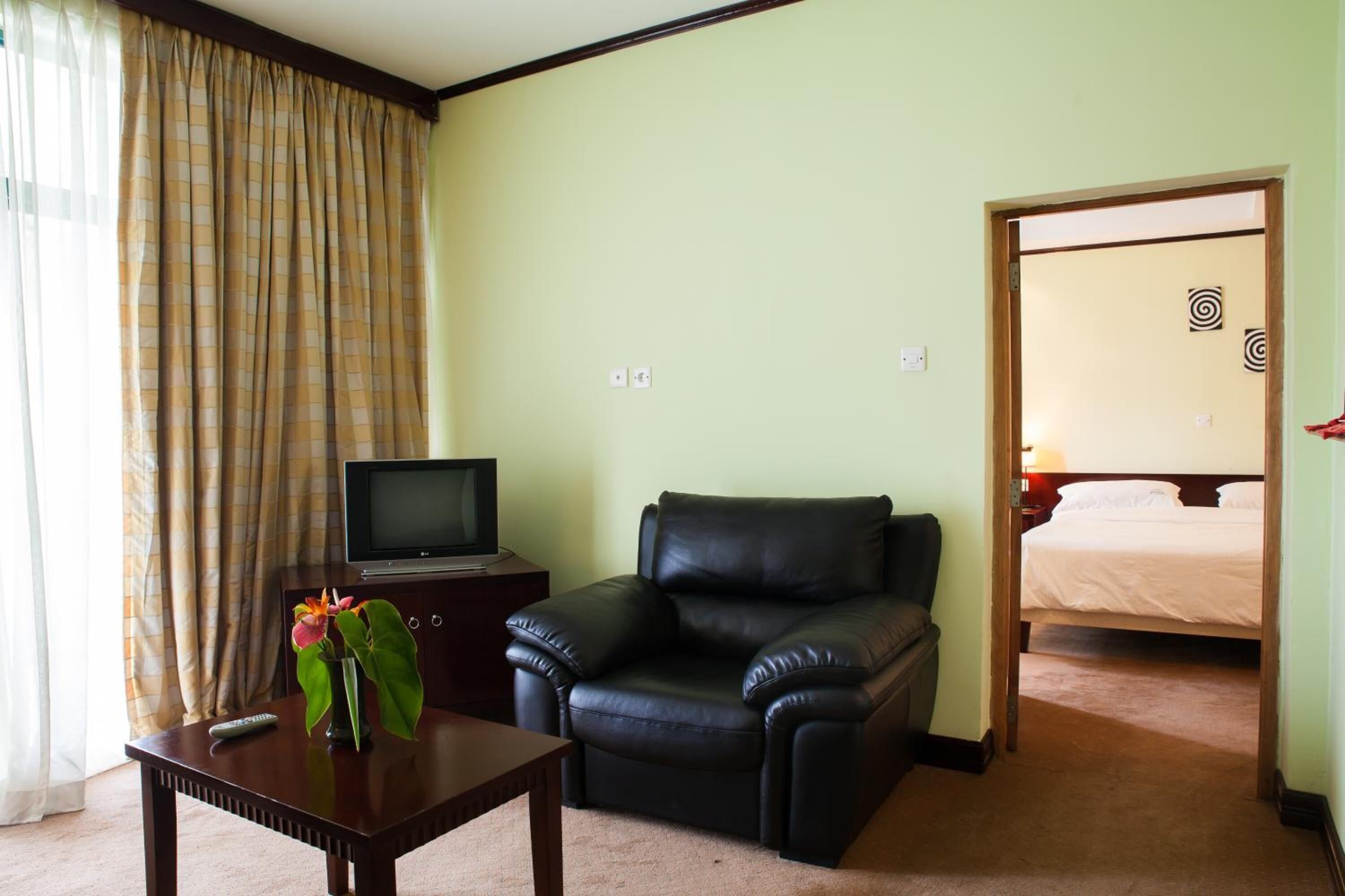 A hotel room with a television on a wooden side table, a black leather chair, a bed with white bedding, and a door leading to another room.