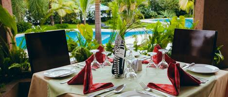 Mesa lista para una comida con vista a una piscina y plantas tropicales.