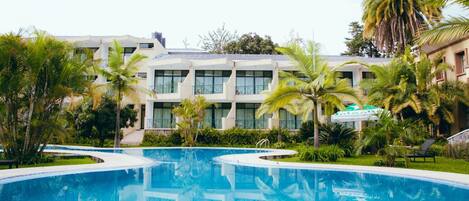 A swimming pool surrounded by palm trees and a building with multiple windows.