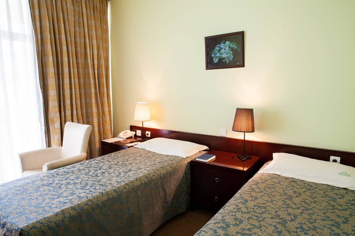 Habitación de hotel con dos camas, una silla, una mesita de noche con lámpara, un teléfono y un cuadro en la pared.