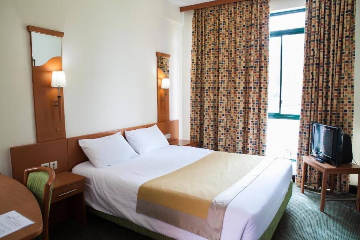 Una habitación de hotel con una cama, mesitas de noche, un escritorio, televisión y cortinas.