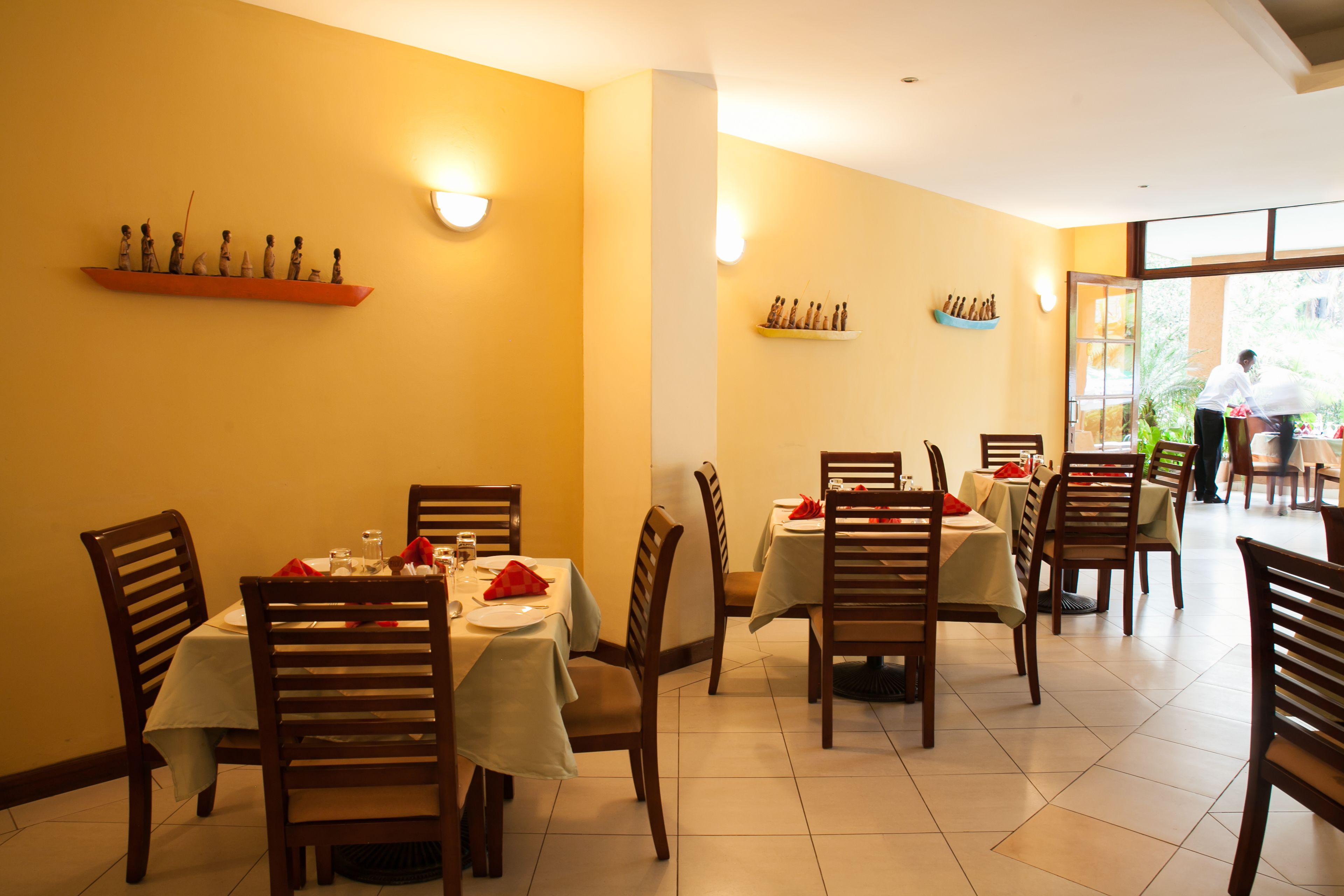A restaurant with wooden chairs and tables, a yellow wall, and a shelf with bottles.
