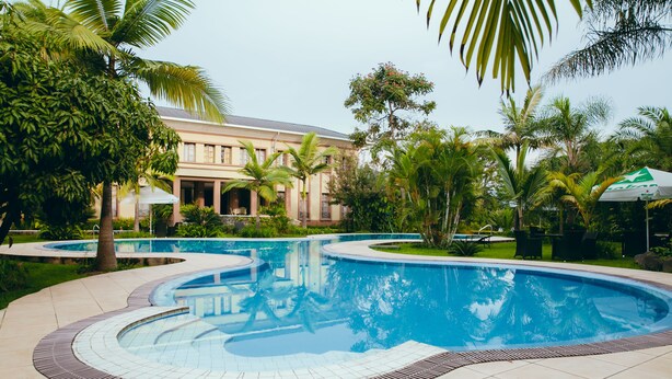Ein Pool mit geschwungener Form, umgeben von Palmen und einem Gebäude mit Säulen.