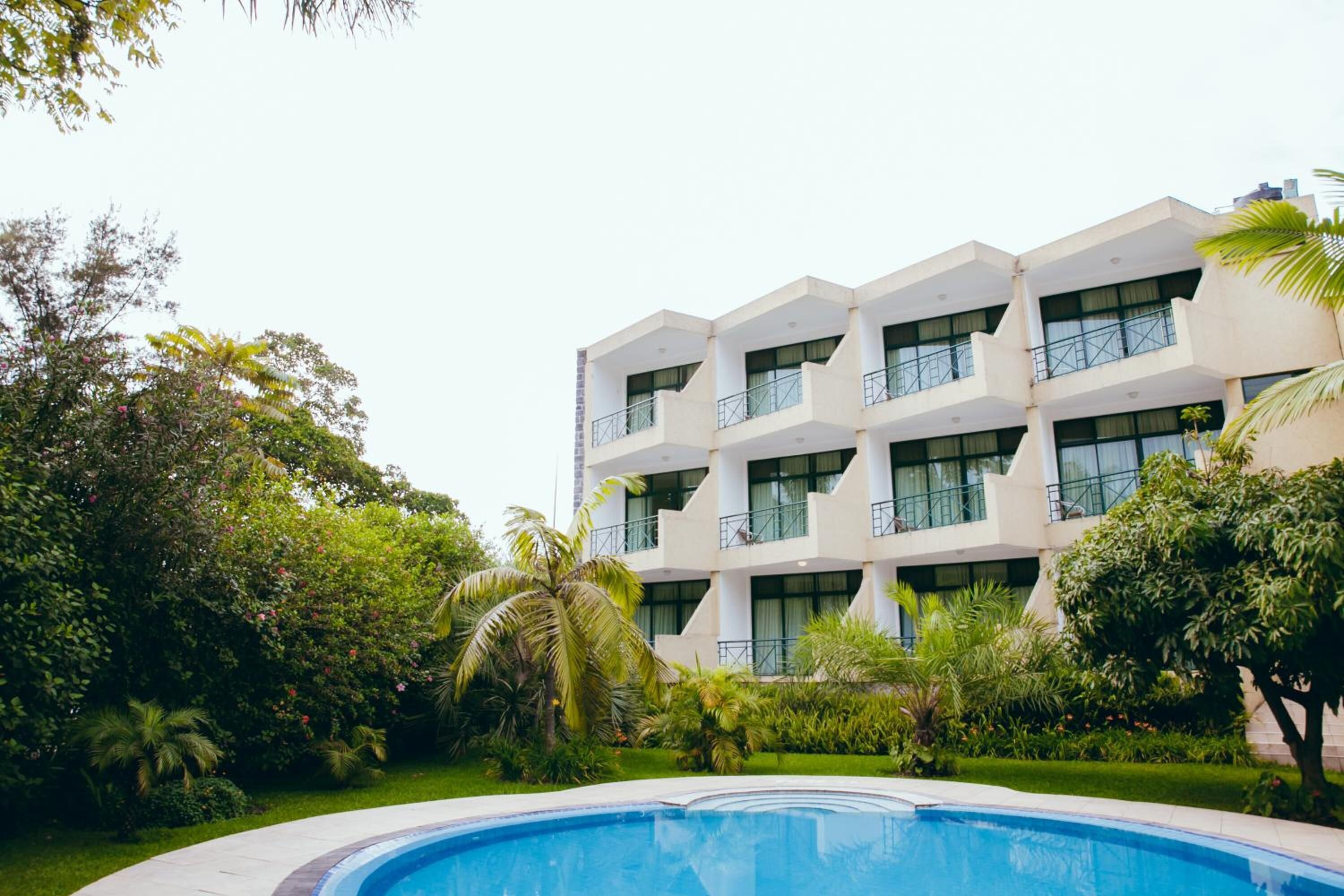 A modern hotel with a pool, surrounded by lush greenery and palm trees.