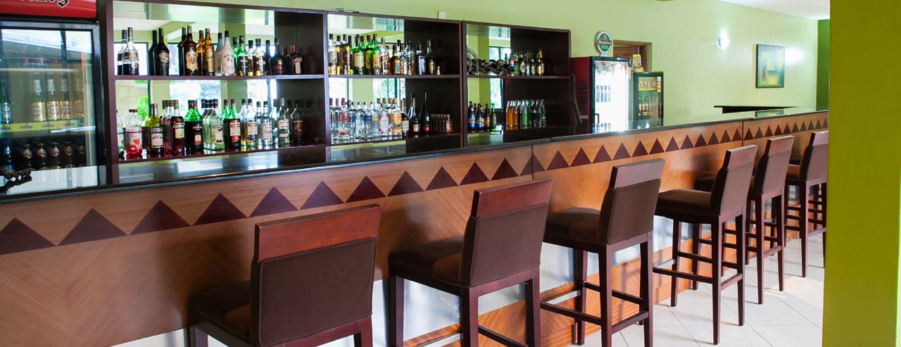 A bar area with multiple shelves of bottles, a counter, and several bar stools.