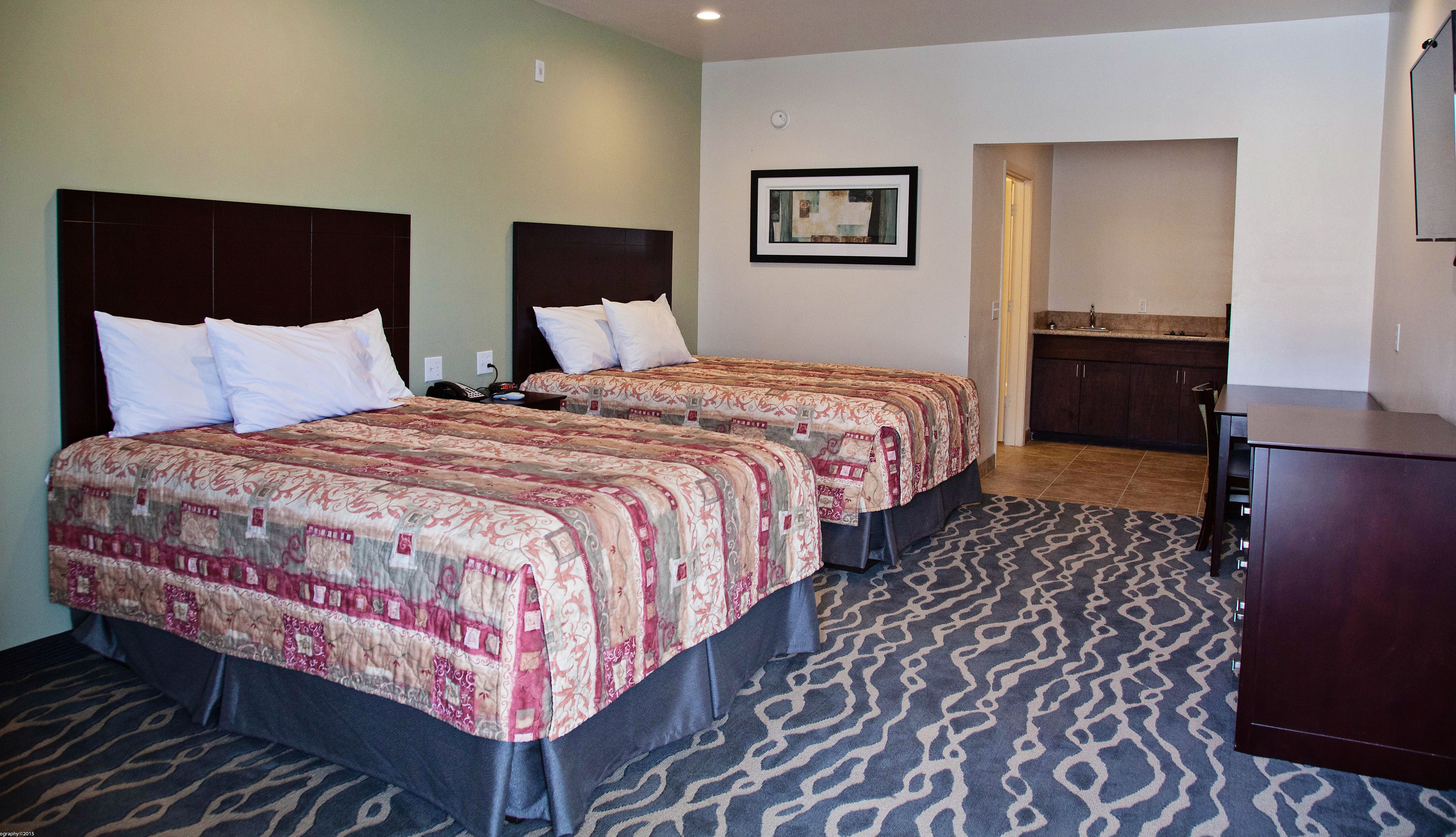 Quarto de hotel com duas camas, uma escrivaninha, uma cadeira, banheiro e cozinha compacta.