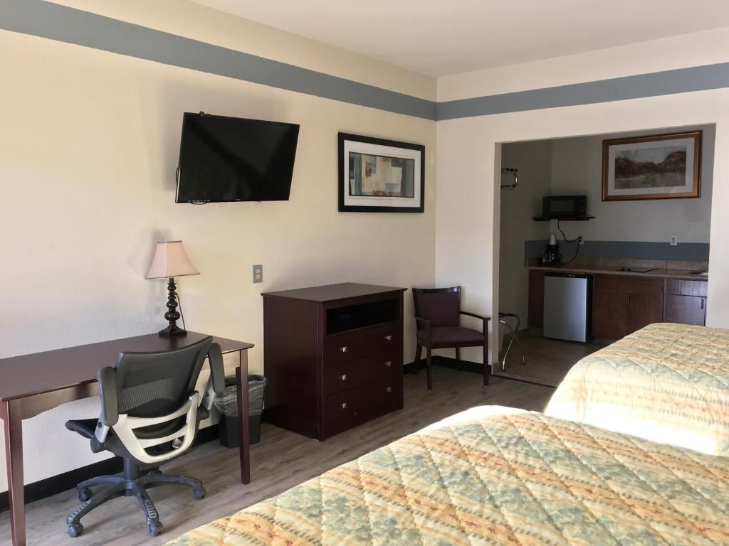 Camera d'albergo con letto, scrivania, sedia, televisione e angolo cottura.