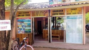 A small building with a sign for a one-day tour, a good luck lanta tour, and a ticket booth. There is a bicycle parked outside. - Funky Fish Hostel (Ko Lanta)
