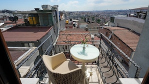 A rooftop terrace with a table, chair, and a vase of flowers.