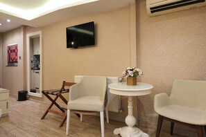 Une pièce avec un téléviseur fixé au mur, deux chaises blanches, une petite table ronde avec un panier, et un radiateur.